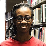 A headshot of Princess Allotey.  She is wearing a red shirt and standing in front of bookshelves.
