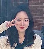 A headshot of Xueyan Liz Cao.  She is wearing a white, long-sleeve shirt and making a peace sign with her right hand.