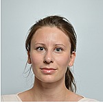 A headshot of Evzenie Coupkova.  She is standing in front of light blue backdrop and wearing a white shirt.