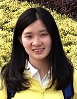A headshot of Longxiu Huang.  She is smiling, wearing a yellow jacket over a white shirt, and standing in front of some bushes.