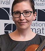 A headshot of Lillian Pierce.  She is wearing glasses and the corner of a violin that she is holding is visible in the picture.
