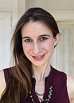 A headshot of Cynthia Rudin.  She is smiling, wearing a sleeveless burgundy shirt, and standing in front of an interior door.