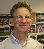 A headshot of Peter Sarnak.  He is wearing a button down shirt and standing in front of a bulletin board.