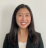 A headshot of Angie Wang.  She is smiling, wearing a black blazer over a white shirt, and standing in front of a light gray backdrop.