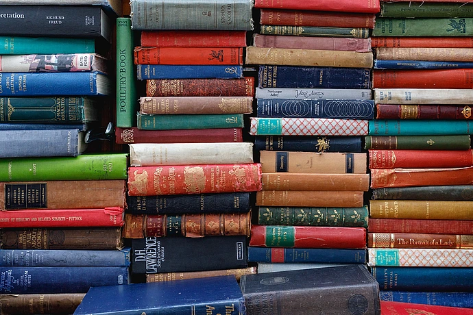 A great number of old, hard-backed books stacked on top of one another.