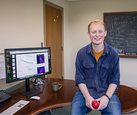 Andy Mummery sitting on the desk of his office in Bloomberg Hall