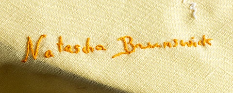 Orange embroidery on a light yellow fabric spells out "Natasha Brunswick" in cursive