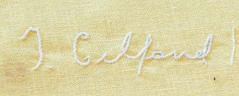 White embroidery of a signature on yellow fabric, showing cursive letters that read "I. Gelfand"