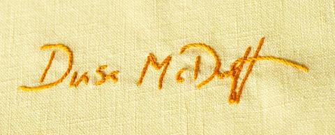 Orange embroidery of a signature on yellow fabric, showing cursive letters that read "Dusa McDuff"