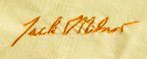 Orange embroidery of a signature on yellow fabric, showing cursive letters that read "Jack Milnor"
